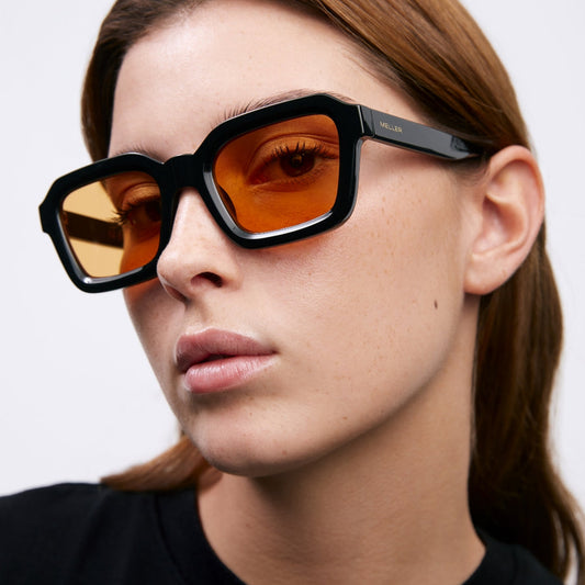 a woman wearing black and orange sunglasses on a white background 
