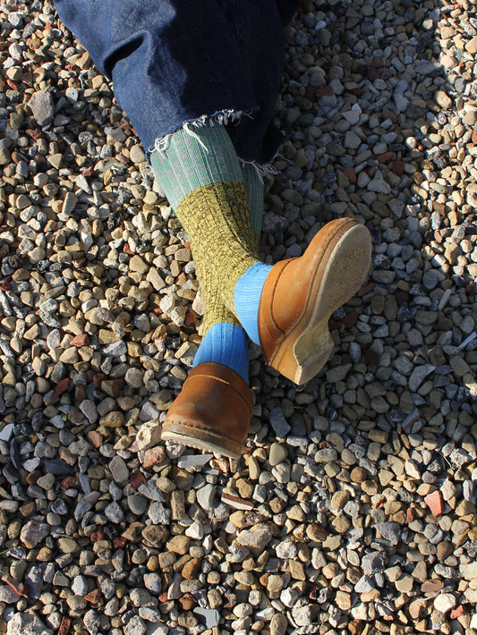 Person wearing brown shoes and multicolored socks on a gravel surface