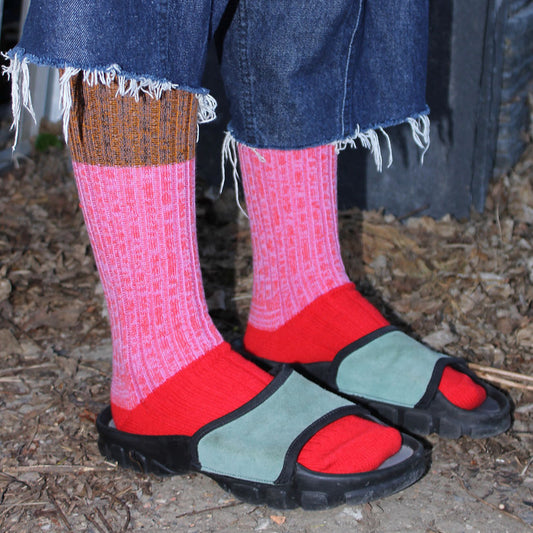 Person wearing pink socks with brown and red accents and sandals on a natural ground surface.
