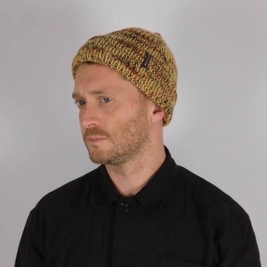 Man wearing a black jacket with a logo and a knitted beanie on a plain background