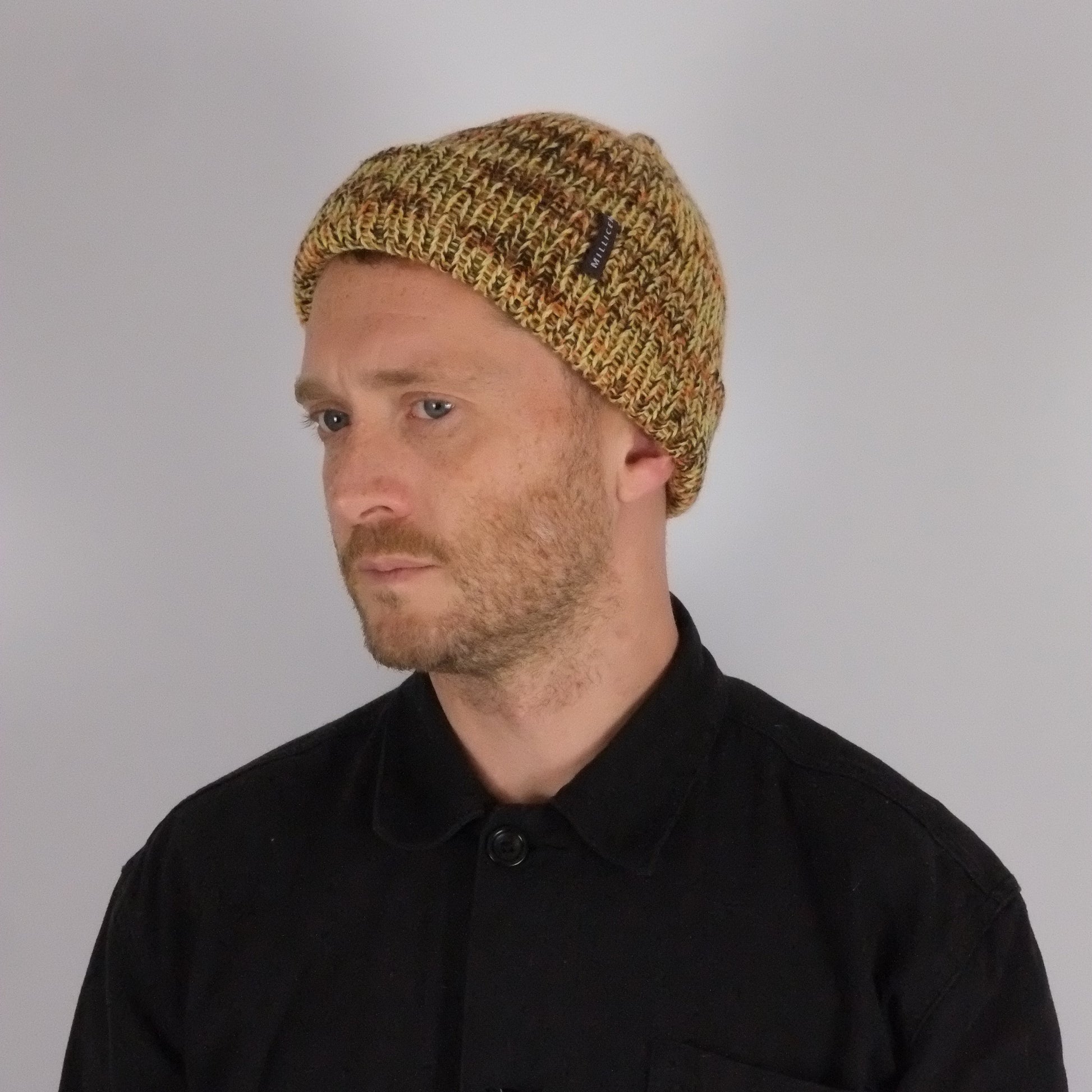 Man wearing a black jacket with a logo and a knitted beanie on a plain background