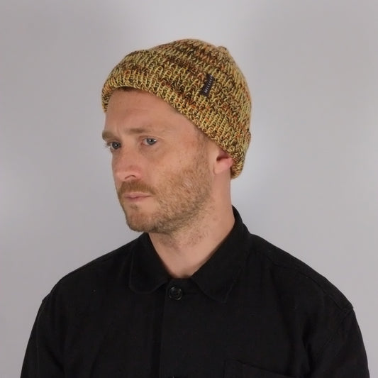 Man wearing a black jacket with a logo and a knitted beanie on a plain background