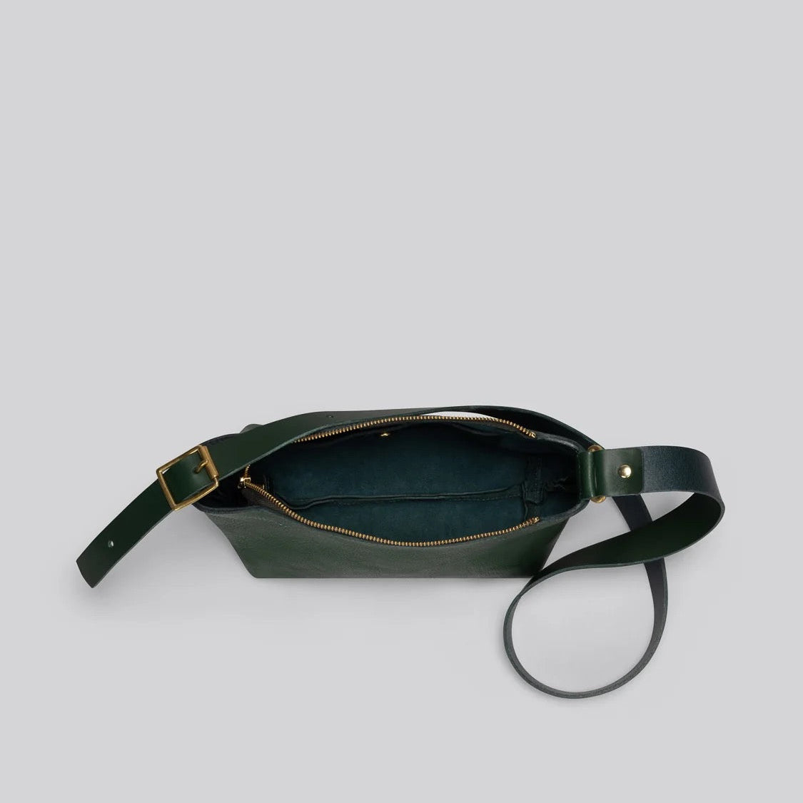 A dark green leather crossbody bag with a gold-tone zipper and hardware, shown open against a solid light gray background.