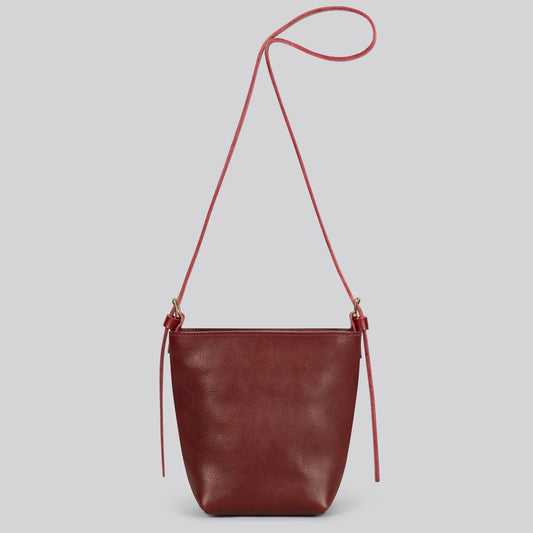 Maroon red leather shoulder bag with a strap on a light gray background