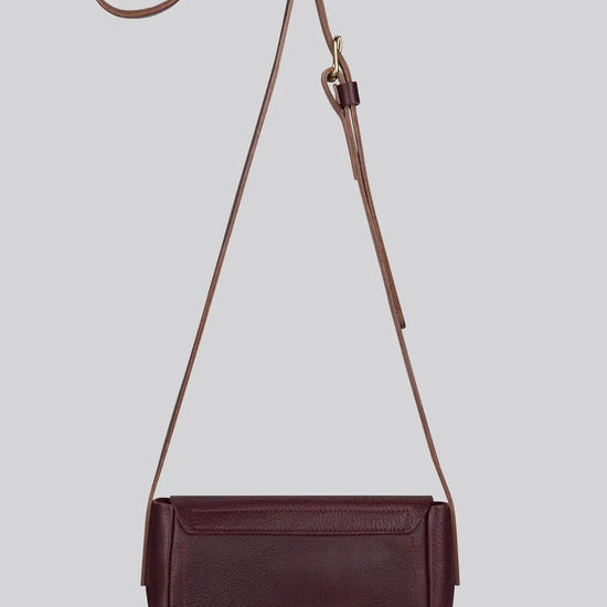 A dark burgundy leather crossbody bag with a matching adjustable shoulder strap, displayed against a solid light grey background.