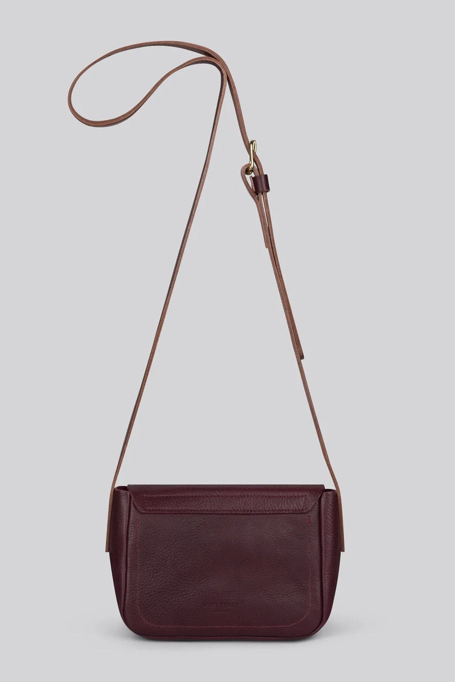 A dark burgundy leather crossbody bag with a matching adjustable shoulder strap, displayed against a solid light grey background.