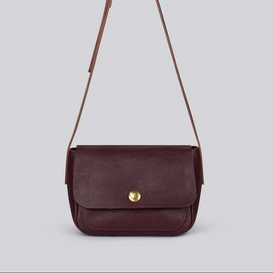 A small dark burgundy leather crossbody bag with a gold snap button and a thin shoulder strap, shown against a solid grey background.