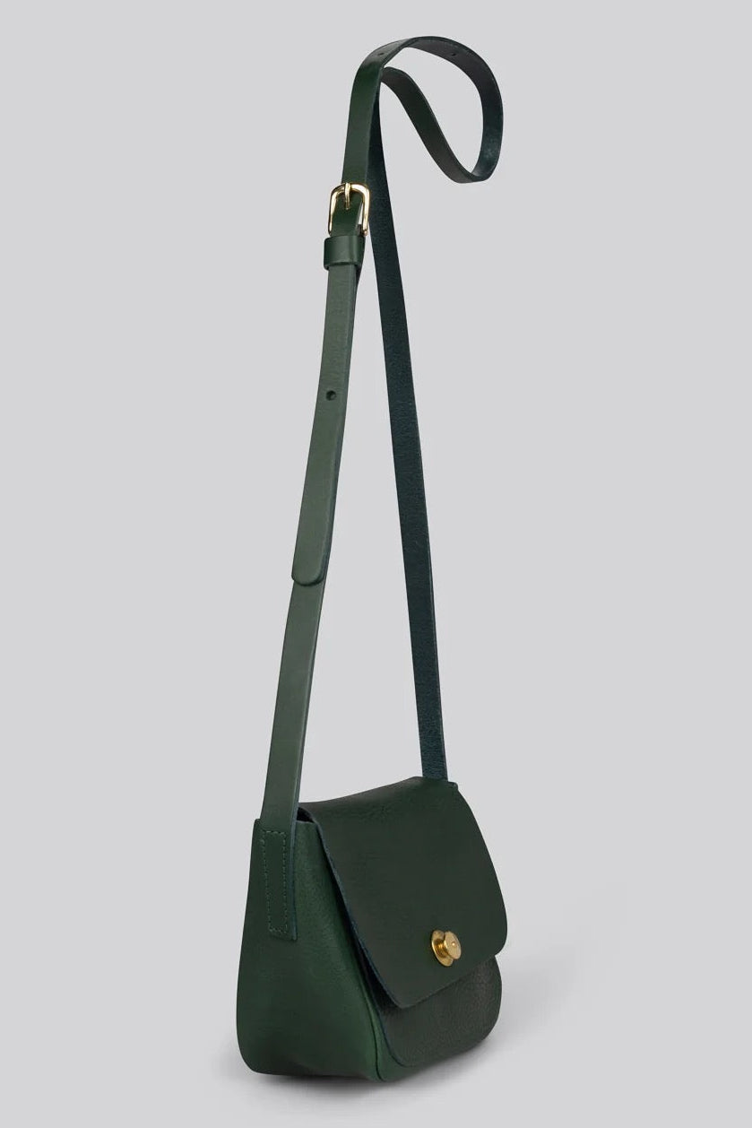 A dark green leather crossbody bag with a long adjustable strap and a small gold-tone turn-lock clasp, shown against a solid light gray background.