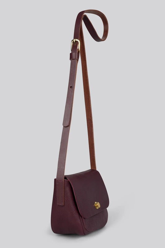 A dark burgundy leather crossbody bag with a matching adjustable shoulder strap and a small gold logo clasp on the front flap, shown against a solid grey background.