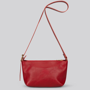 A red pebbled leather crossbody bag with a thin matching shoulder strap and gold-tone hardware, shown against a solid gray background.