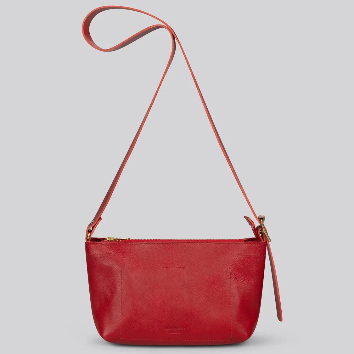 A red leather crossbody bag with a long adjustable strap and gold-tone hardware, shown against a solid light gray background.