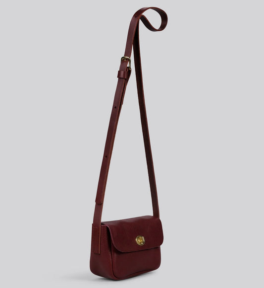 Maroon red  leather crossbody bag with brass clasp on a light gray background
