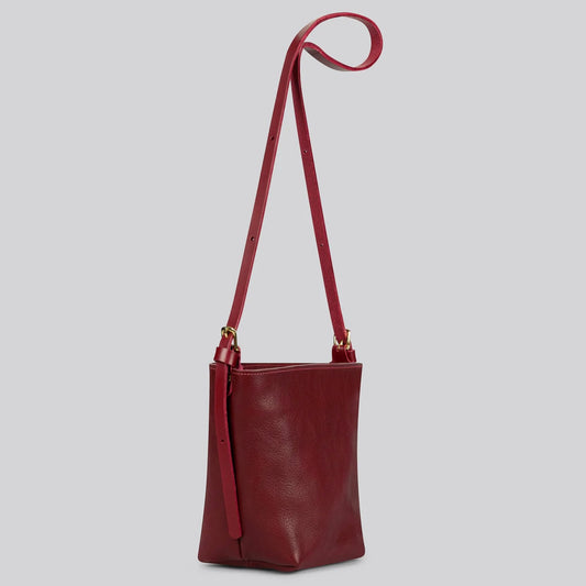 Red handmade leather handbag with a strap on a light gray background