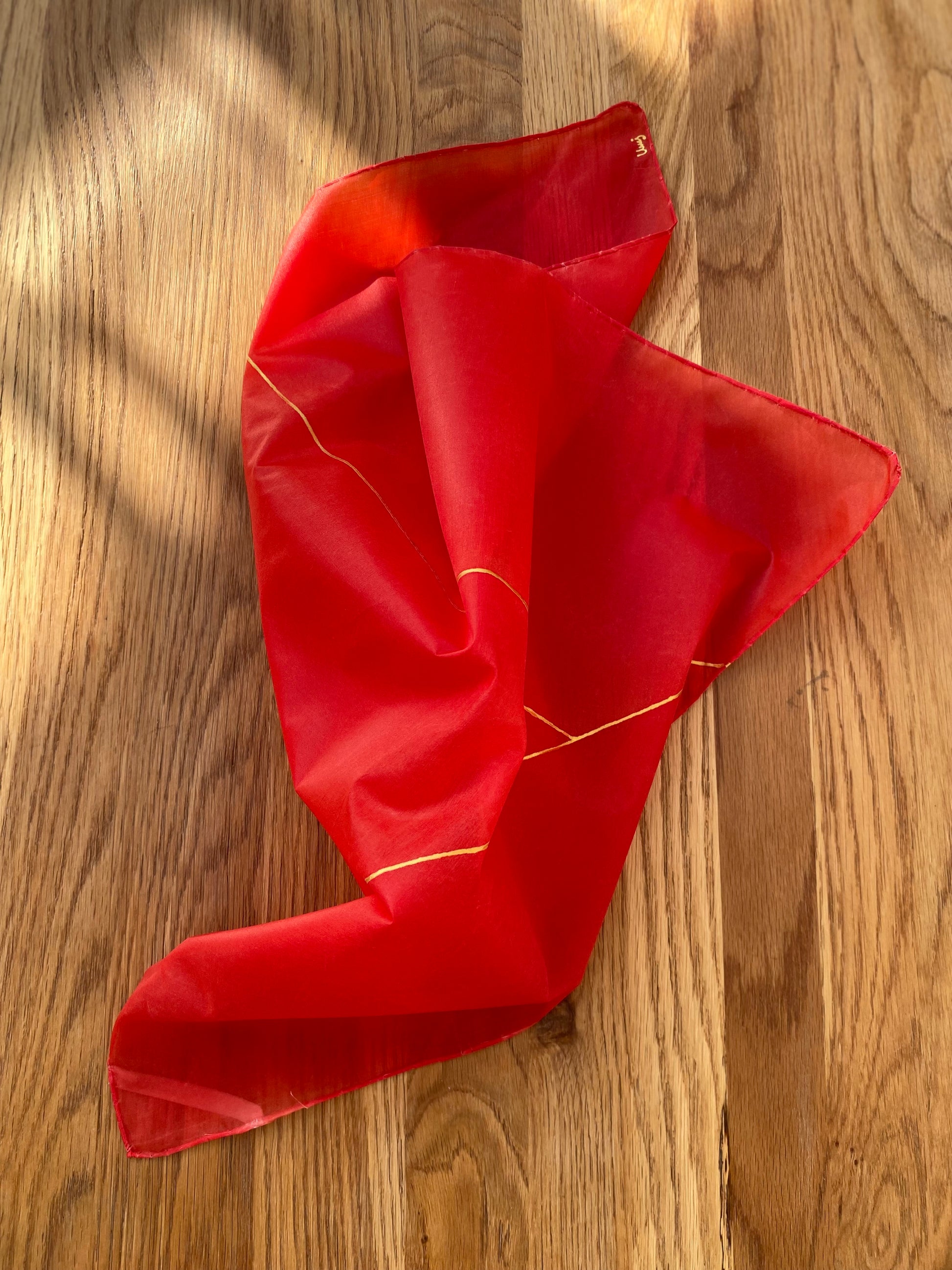 Red silk scarf with gold trim on a wooden surface