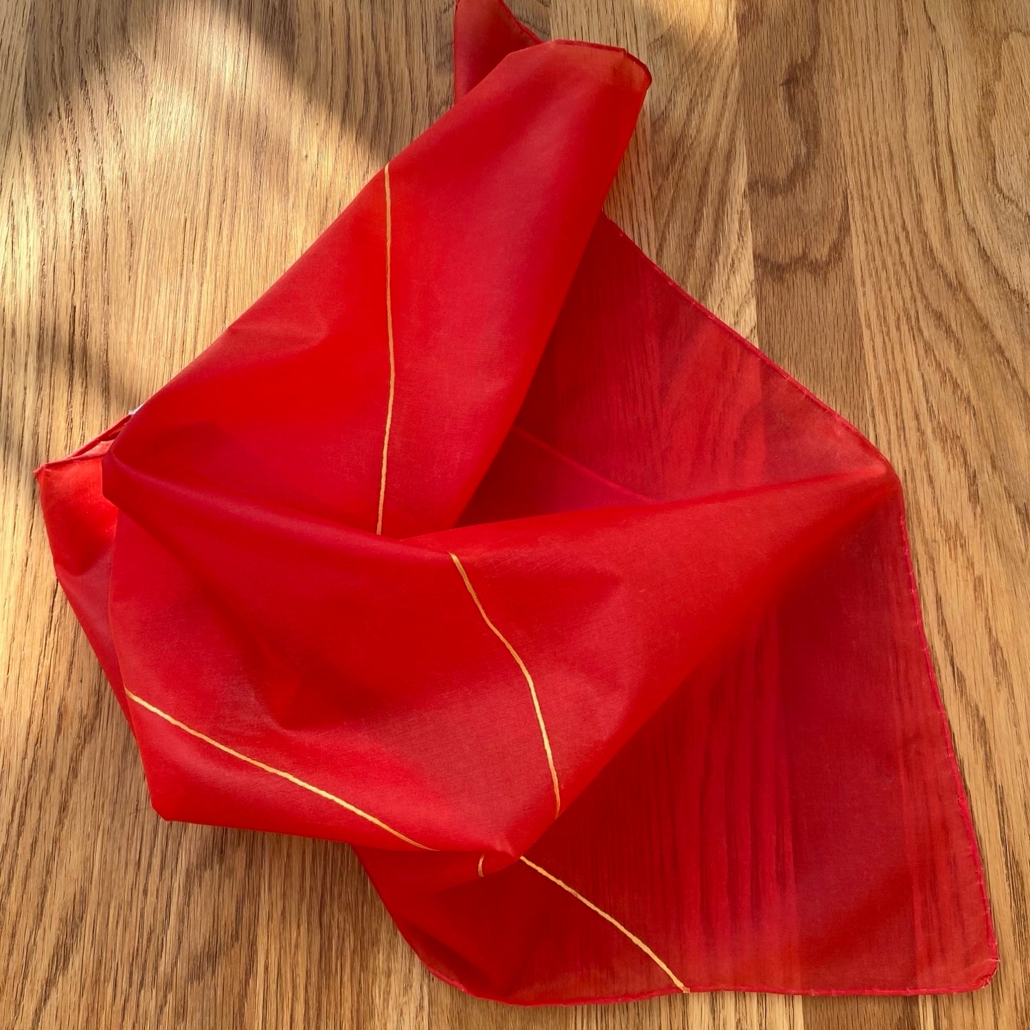 Red silk scarf with gold trim on a wooden surface