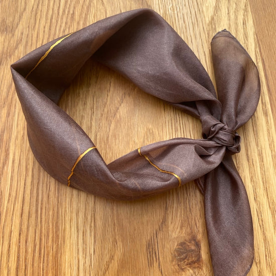 Brown silk scarf with gold trim on a wooden surface