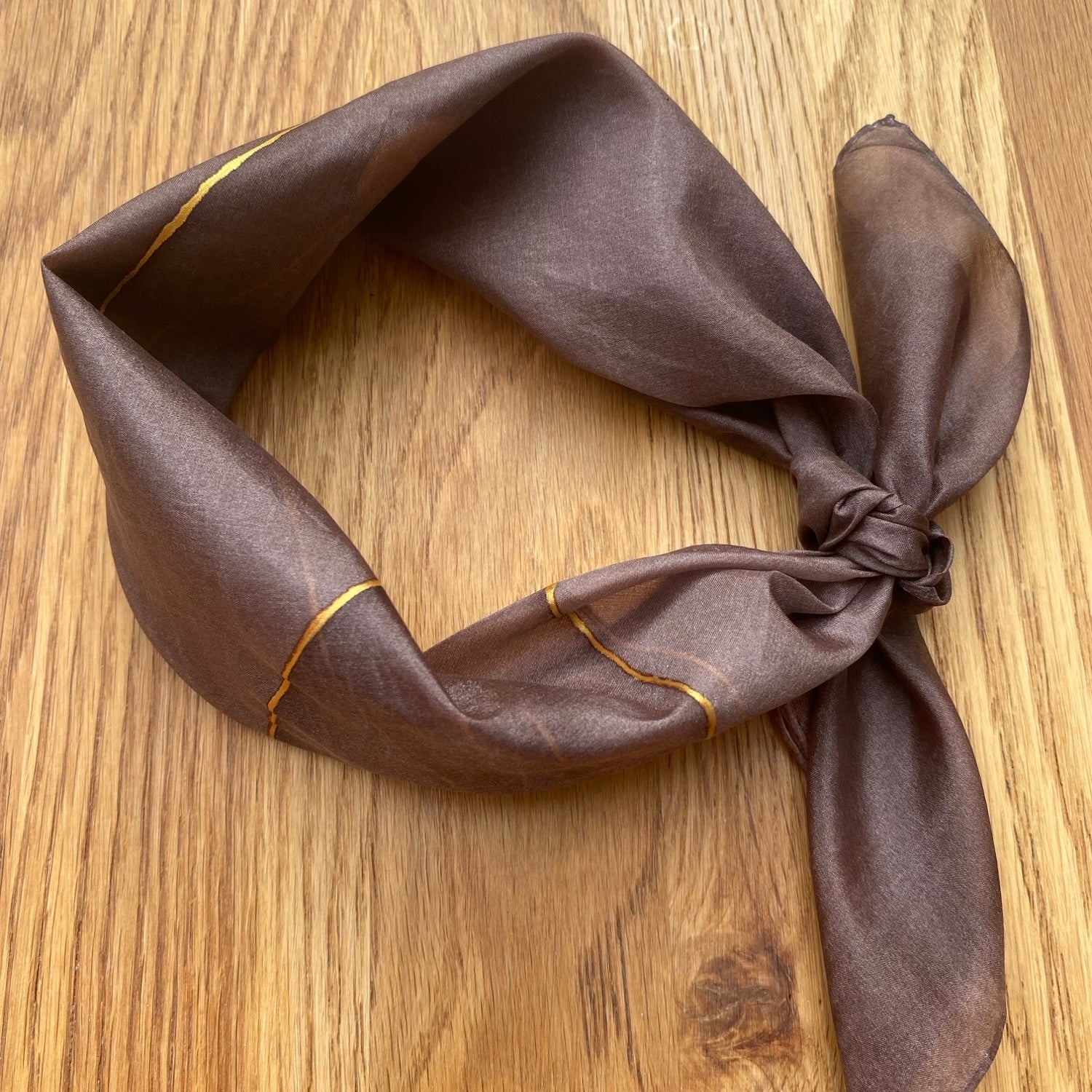 Brown silk scarf with gold trim on a wooden surface