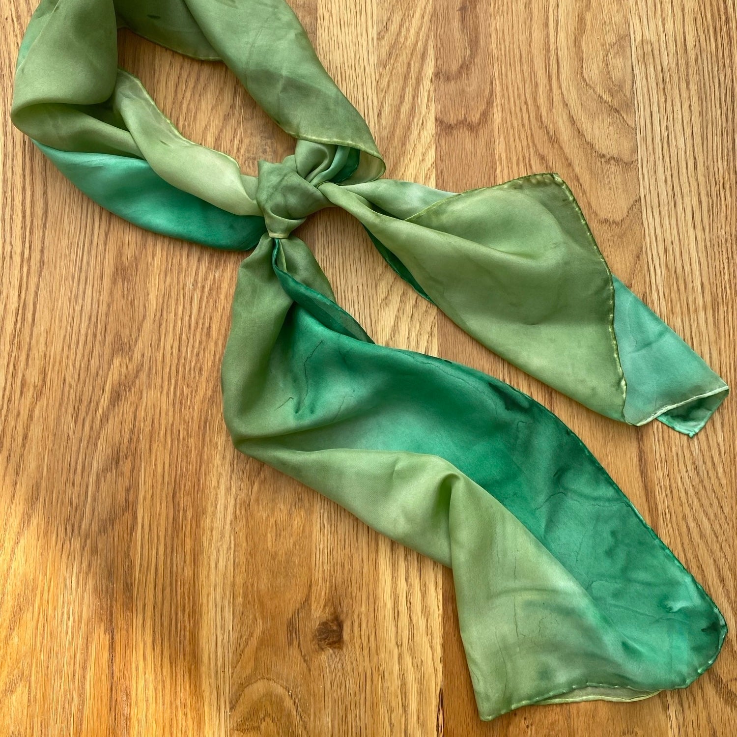 Long green silk scarf with knot on wooden background 