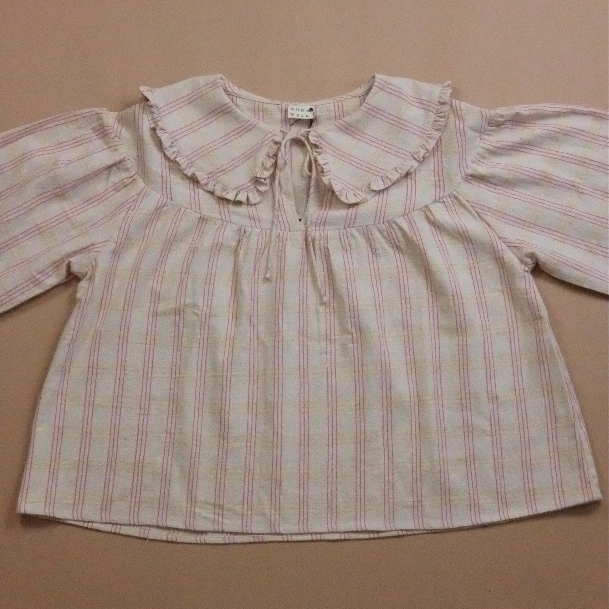 Striped blouse with ruffled collar and tie neck on a beige background