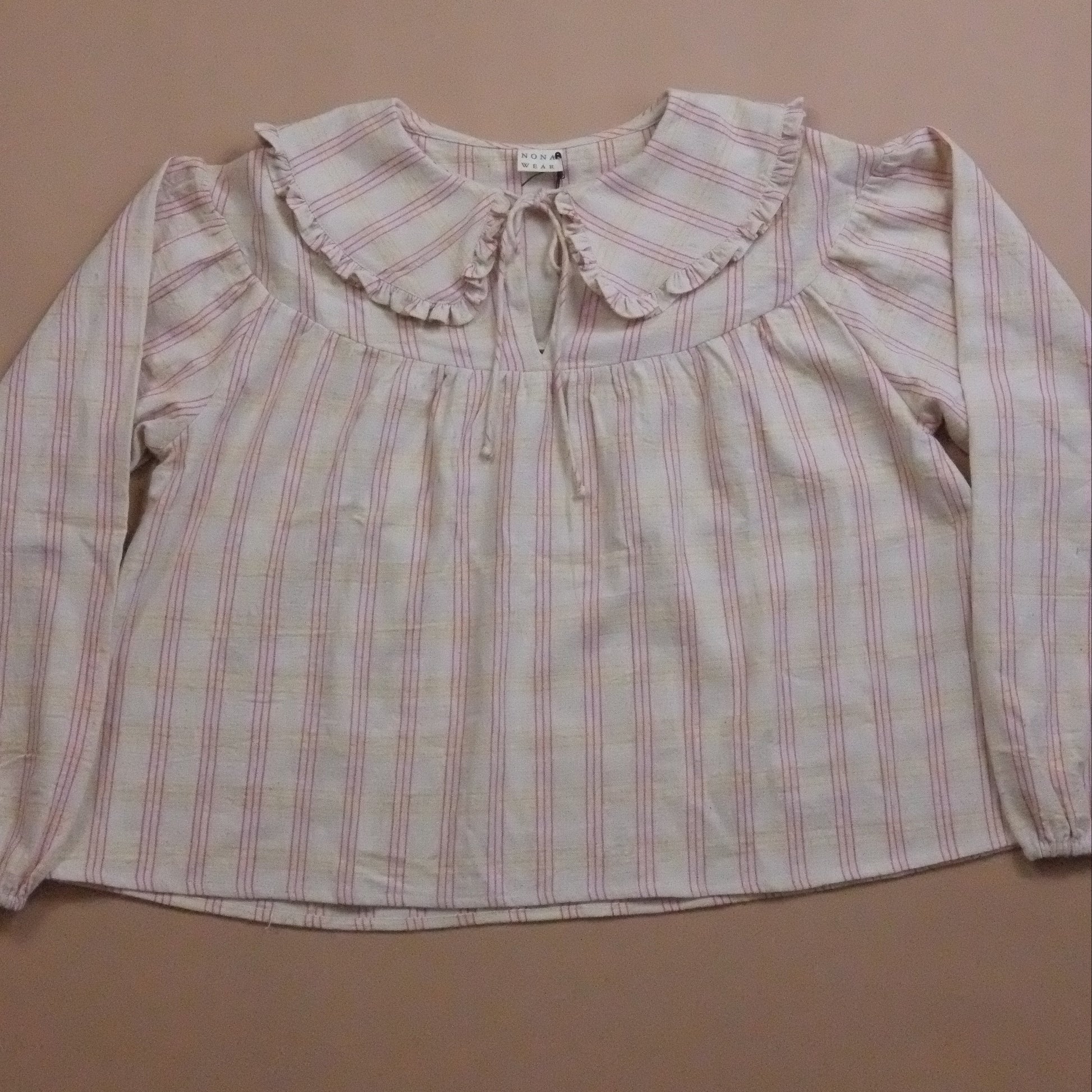 Plaid blouse with ruffled collar and tie neck on a beige background