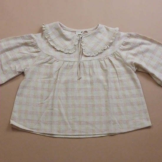 Plaid blouse with ruffled Peter Pan collar and tie neck on a beige background