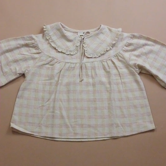 Plaid blouse with ruffled Peter Pan collar and tie neck on a beige background