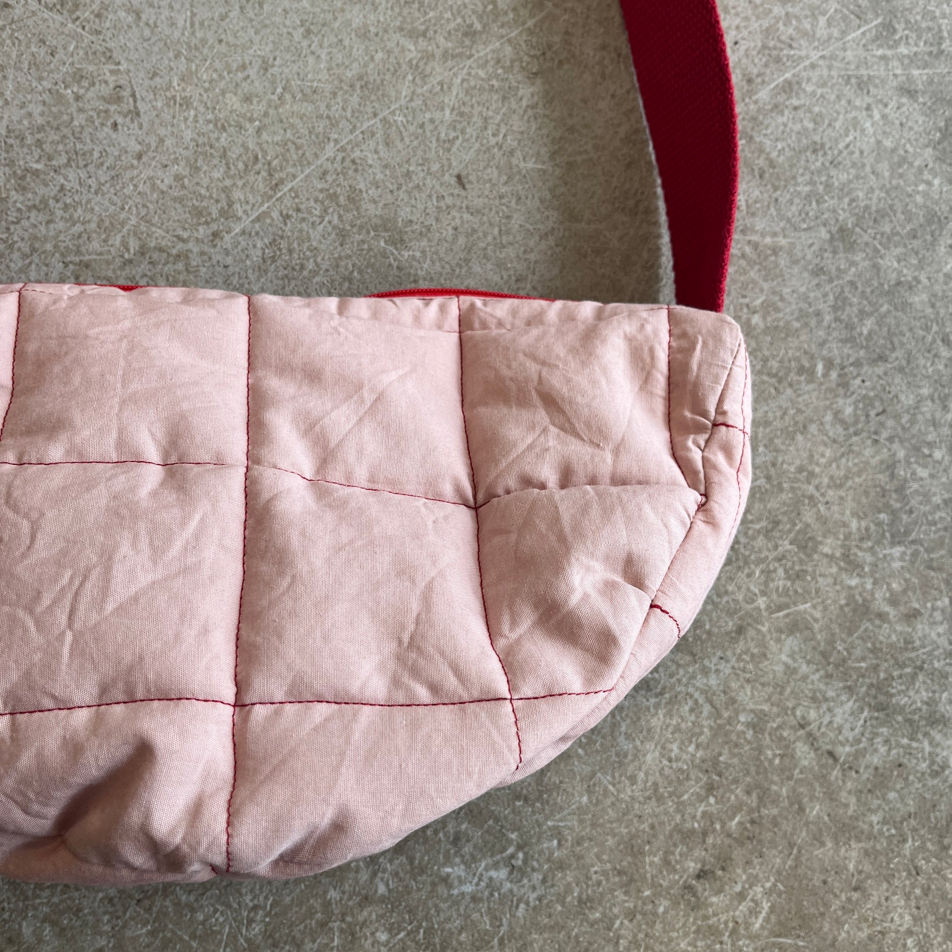 Pink quilted bag with red stitching on a gray surface