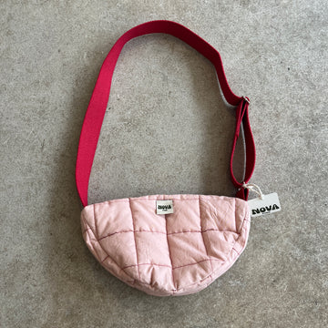 Pale pink cotton padded cross body bag with adjustable strap and zip on grey concrete background