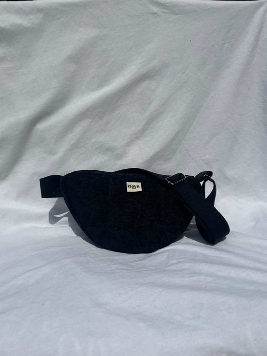 A black fabric cross body bag with a small white brand label reading 'BAGGA' on a wrinkled white fabric background.