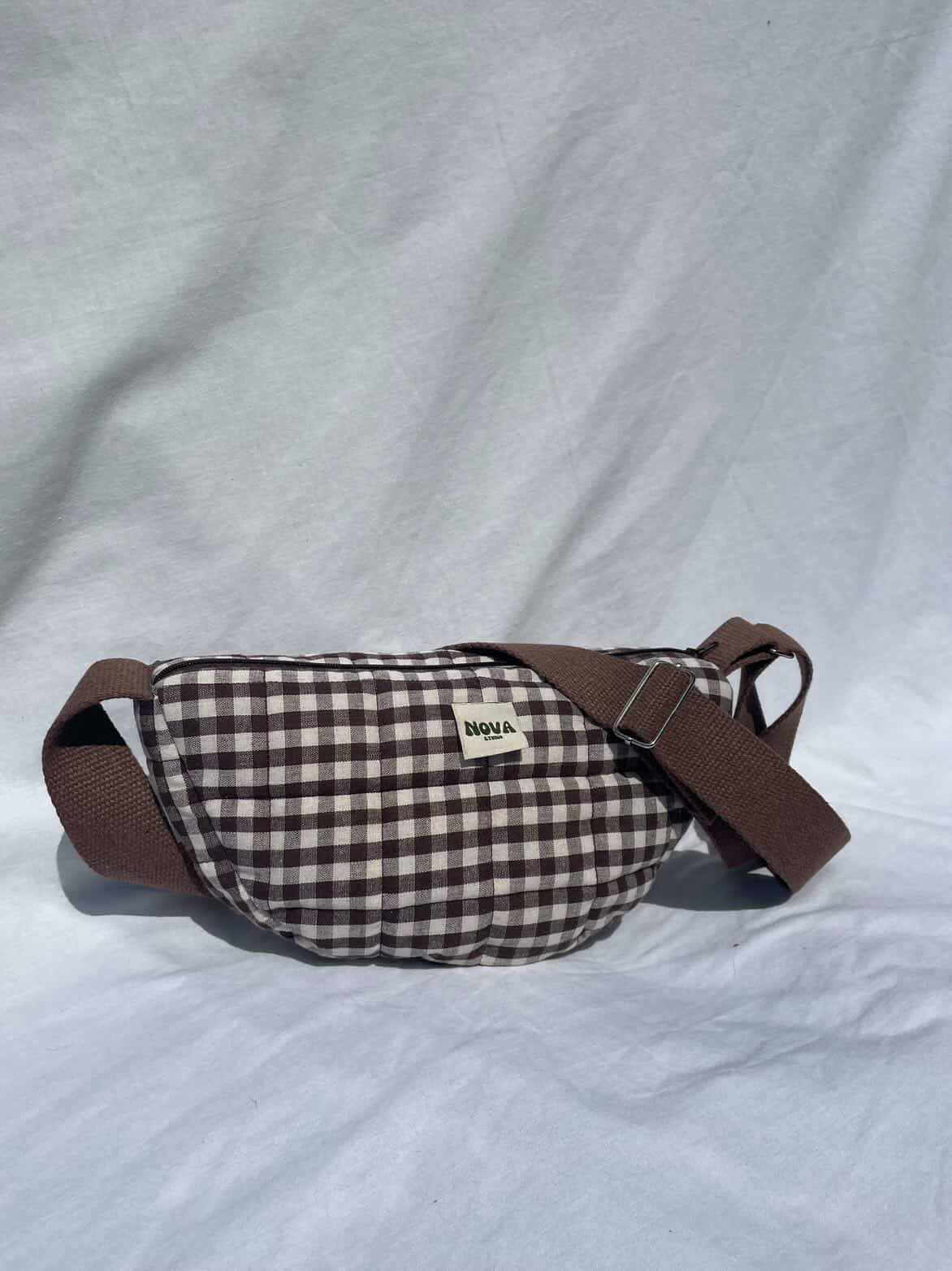 Plaid-patterned waist bag with brown strap on a light gray background