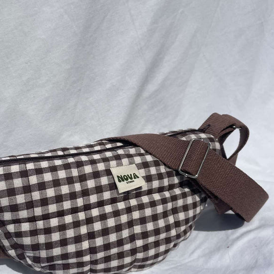 Brown and white checkered bag with a brown strap on a light gray background