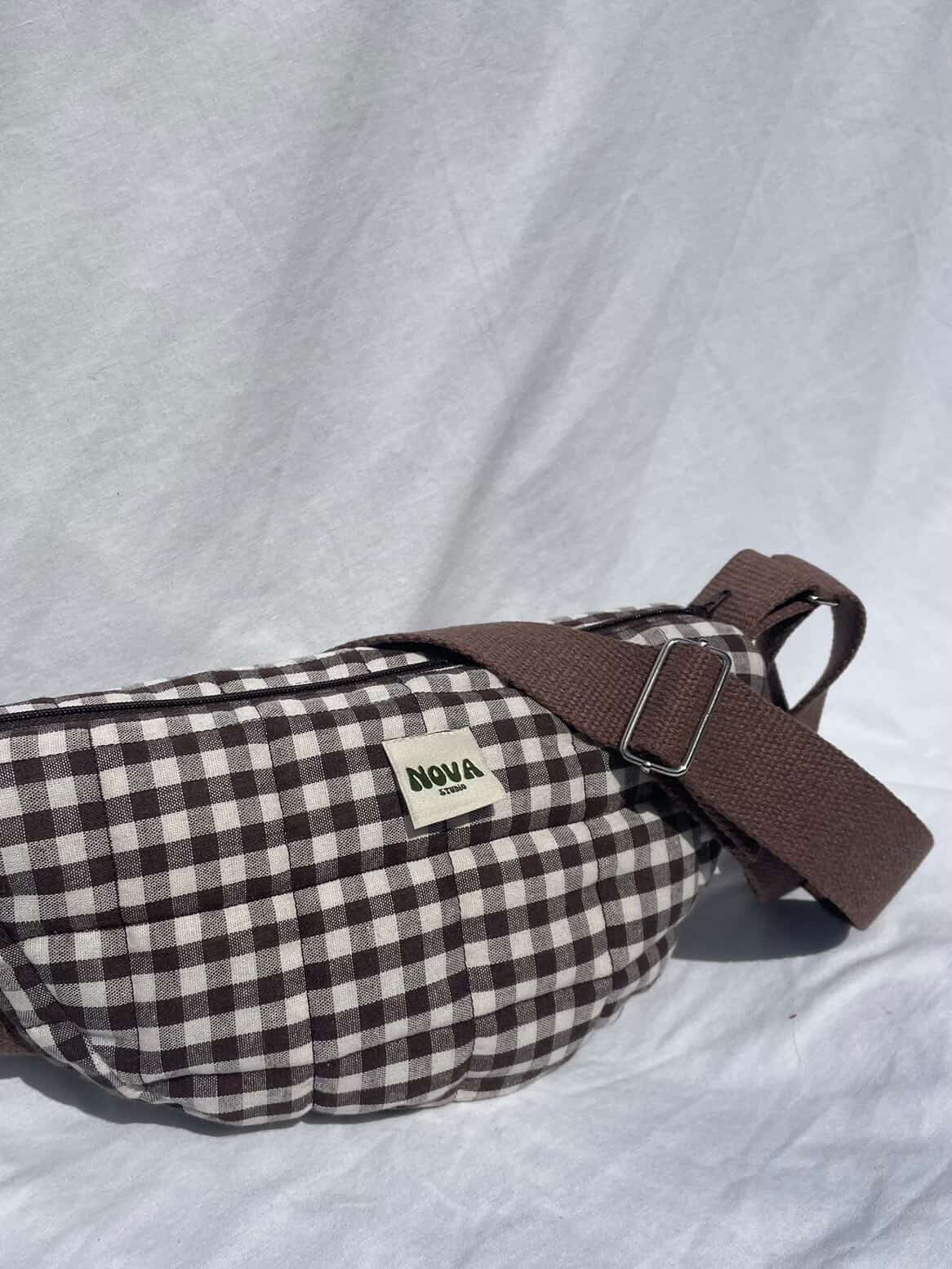 Brown and white checkered bag with a brown strap on a light gray background