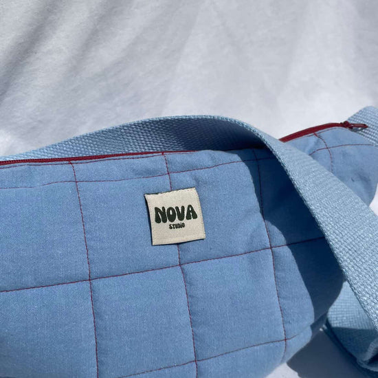 Blue quilted bag with 'NOVA' label on a white background