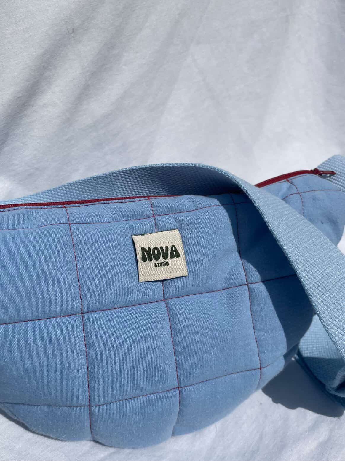Blue quilted bag with 'NOVA' label on a white background