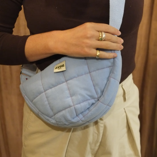 A person wearing a light blue quilted crossbody bag with a matching strap, styled with a dark brown long-sleeve top and beige pants.
