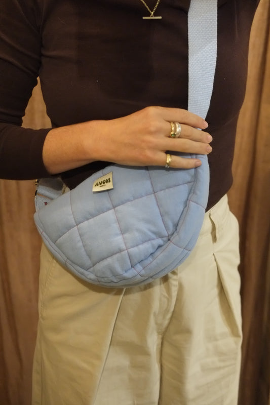 A person wearing a light blue quilted crossbody bag with a matching strap, styled with a dark brown long-sleeve top and beige pants.