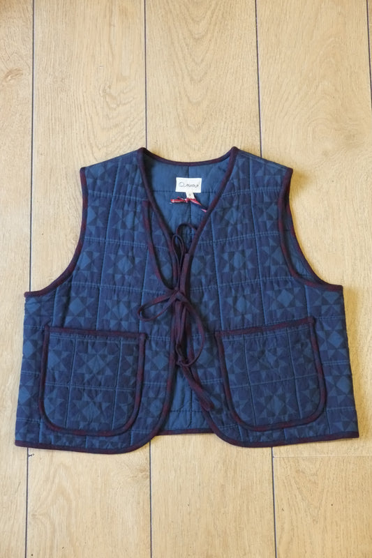 Navy and cornflower blue patchwork quilted waistcoat with burgundy trim and two front ties on a light wooden background
