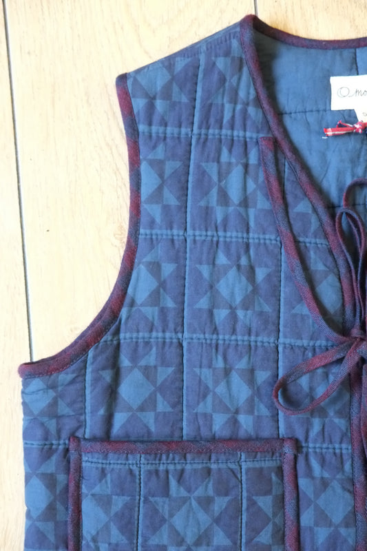 Navy and cornflower blue patchwork quilted waistcoat with burgundy trim and two front ties on a light wooden background