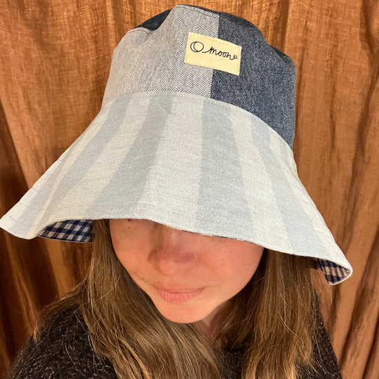 Person wearing a striped bucket hat with a large brim in front of a brown curtain
