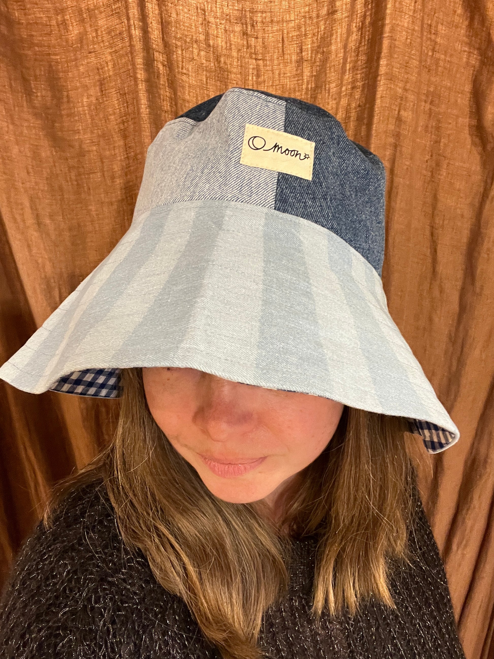 Person wearing a striped bucket hat with a large brim in front of a brown curtain