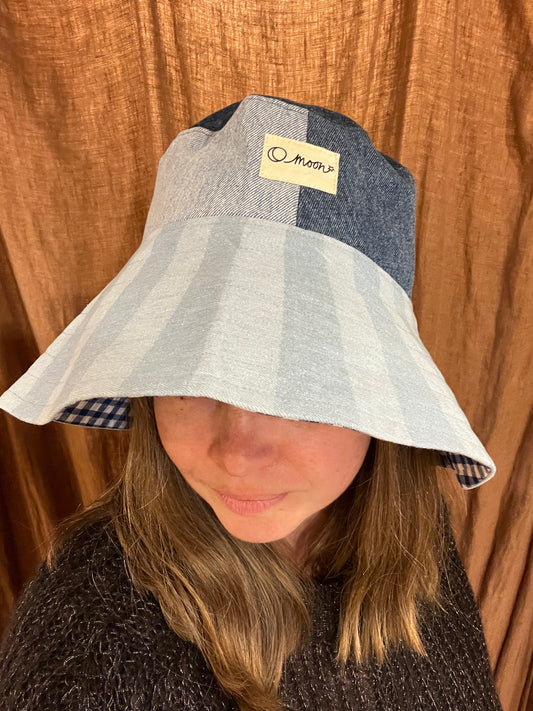 Person wearing a striped bucket hat with a large brim in front of a brown curtain