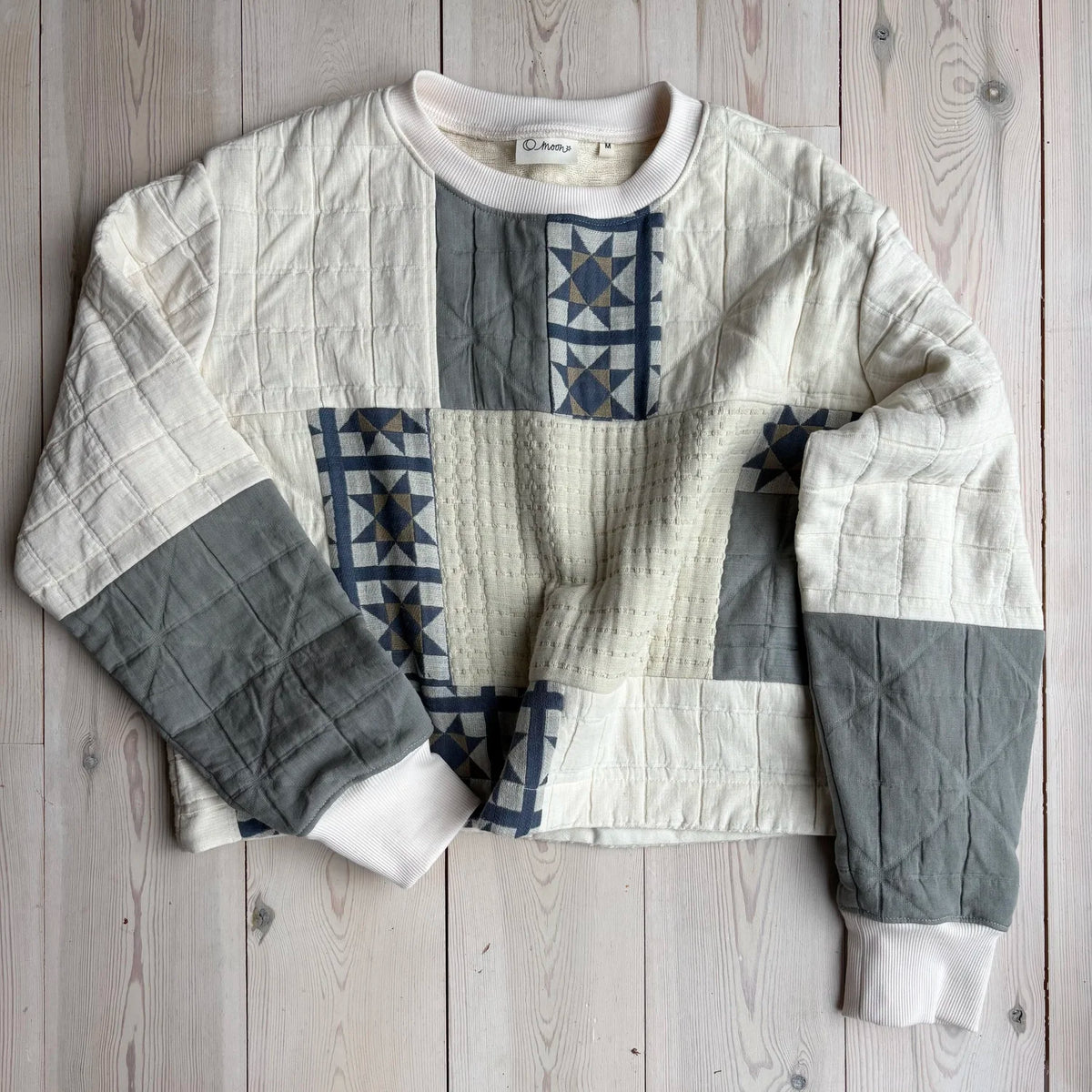 an ecru sweatshirt with patchwork detailing on a wooden background 
