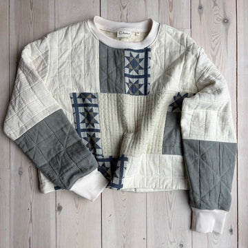 an ecru sweatshirt with patchwork detailing on a wooden background 
