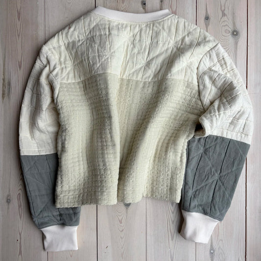 The back of an ecru jumper with patchwork detailing on a wooden floor 