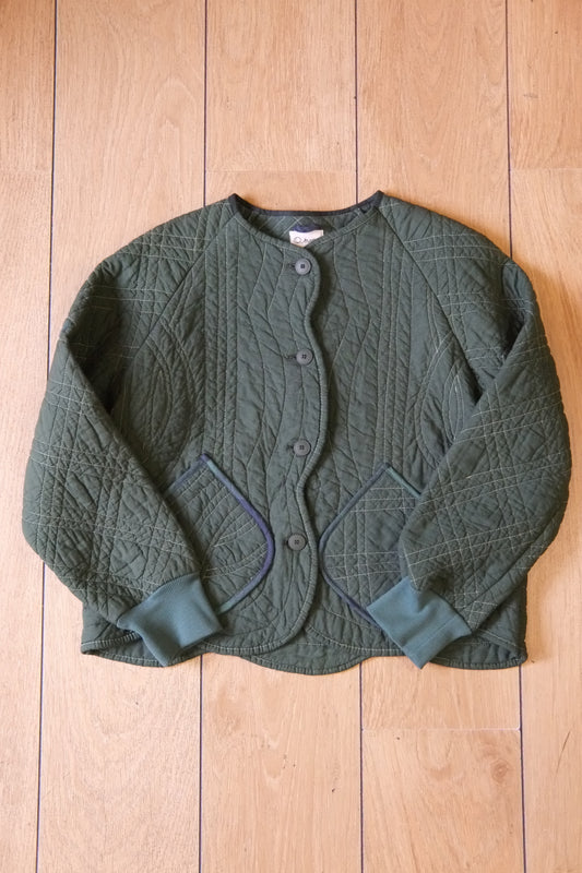 A green quilted cardigan jacket with button closure and ribbed cuffs, laid flat on a light wood plank background.