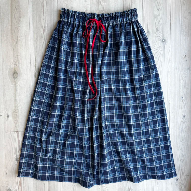 Blue plaid pajama pants with a red drawstring on a wooden surface