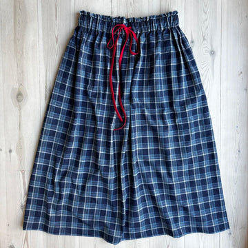 Blue plaid pajama pants with a red drawstring on a wooden surface