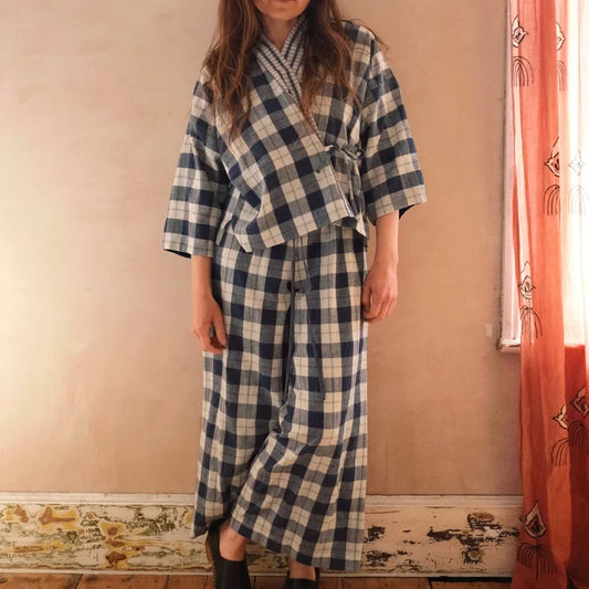 Person wearing a blue and white checkered outfit standing in a room with a pink wall and orange curtain.