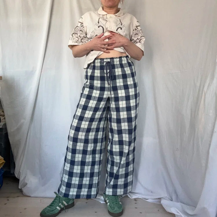 Person wearing a white patterned shirt and blue plaid drawstring trousers against a plain background