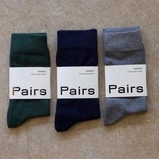 Three pairs of socks in green, navy, and grey with 'Pairs' labels on a beige surface.